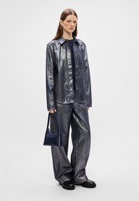 Conjunto de camisa e calças oversized cinza metálico com uma bolsa azul. Apresenta uma frente de botões e pernas largas, feito de um tecido suave e texturado.