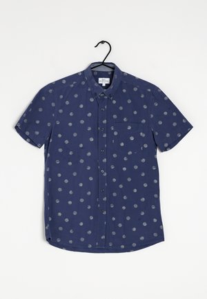 Camisa de manga corta en tejido azul marino con patrones circulares grises, cuello abotonado y bolsillo en el pecho izquierdo. Textura suave, diseño informal.