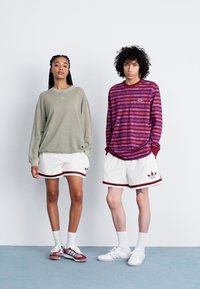 Grøn oversized sweatshirt, hvide teksturerede shorts med maroon accenter; maroon og lilla stribede langærmede skjorte, hvide shorts med lignende accenter.