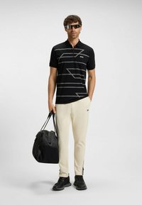 Czarna koszulka polo z szarymi ukośnymi paskami, połączona z białymi spodniami o zwężonym kroju. Czarna torba podróżna i sportowe czarne buty. Noszone okulary przeciwsłoneczne w stylu kompozytowym.