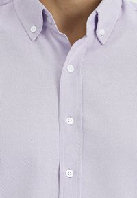 Camicia button-up viola chiaro con tessuto testurizzato, caratterizzata da un colletto a punte e bottoni bianchi. Dettagli di cucitura visibili in tutto il capo.