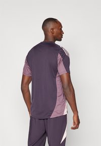 Maillot de sport à manches courtes avec un corps violet foncé, des panneaux latéraux violet clair et trois rayures blanches sur les épaules.