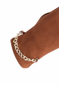 Borsa in faux suede marrone con tracolla in catena dorata e dettaglio in pelle. La texture è liscia con una finitura opaca.