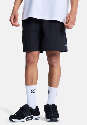 Czarne szorty o lekkiej fakturze, z logo na lewej nodze, zestawione z czarnymi butami i białymi skarpetkami z logo. Casualowy, sportowy styl.