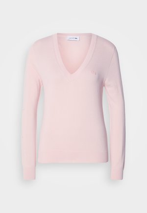 Šviesiai rožinė V-kaklo megztinis pagamintas iš minkštos medžiagos, turi ilgus rankovės, raukšlėtus išpjaustymus ir mažą siuvinėtą logotipą ant krūtinės.