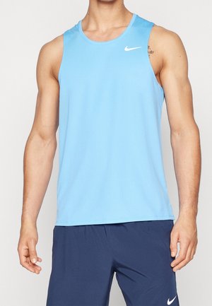 Homme portant un débardeur de sport bleu clair et un short bleu foncé, tous deux avec des logos Nike blancs, debout devant un fond uni.