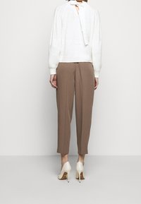 Pull en maille blanche avec un détail de nouage au dos, associé à un pantalon marron ample et des chaussures à talons crème. Textures douces sur l'ensemble.
