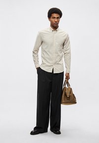 Ανοιχτό μπεζ πουκάμισο με κουμπιά, μαύρο φαρδύ παντελόνι και καφέ τσάντα. Λεπτό ύφασμα, δομημένη σιλουέτα και casual στυλ.