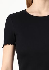 Čierny rebrovaný top s krátkym rukávom, okrúhlym výstrihom a vlnitými okrajmi na rukávoch, vyrobený z mäkkej, elastickej látky.
