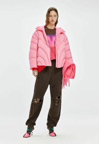 Puffige roze jas met een doorgestikt ontwerp, gedragen over een gradient sweater, gecombineerd met bruine ripped broek en kleurrijke hakken. Houdt een roze sjaal vast.