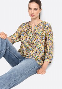 Colorful, lightweight blouse with a v-neck and ¾ sleeves. Patterned with small dots in blue, green, yellow, and brown on a light background.