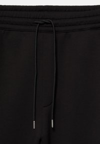 Taille de pantalon de jogging noire avec un cordon noir noué et des embouts métalliques aux extrémités.