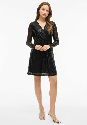 Robe noire courte avec de longues manches transparentes ; présente un décolleté en V profond et une taille cintrée. Le tissu a une texture brillante et pailletée.