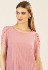 Helle rosa Bluse mit plissierter Textur, kurzen, flatterhaften Ärmeln und Rundhalsausschnitt, aus weichem, fließendem Stoff gefertigt.