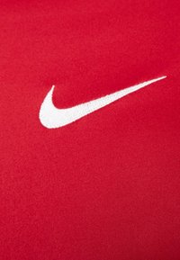 Rødt stof med en glat tekstur har et fremtrædende hvidt Nike swoosh-logo. Ingen yderligere mønstre eller detaljer til stede.