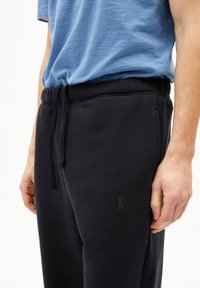 Pantalons de survêtement noirs avec poches latérales, taille élastique et cordon de serrage. Le tissu semble doux avec une texture uniforme.