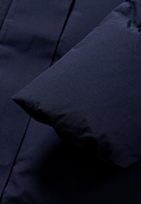 Detalle de una chaqueta acolchada azul marino, con una textura de tela suave, un diseño de mangas suaves y esponjosas, y costuras cosidas.