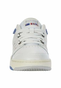 Sneaker bianco con superiore in pelle liscia, accenti blu, laccio visibile, colletto imbottito e suola in gomma testurizzata. Presenta il logo del marchio e bandiere nazionali.