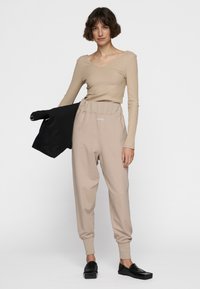 Helles beiges, eng anliegendes Langarmshirt mit gerippter Textur, kombiniert mit lockeren, hellbeigen Jogginghosen mit elastischem Bund und seitlichen Taschen.