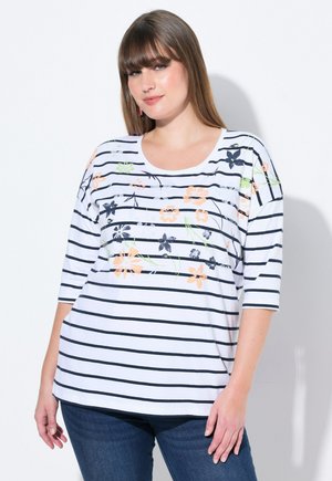 Haut rayé blanc avec des rayures bleu marine, présentant des motifs floraux en orange et vert. Col bateau et manches trois-quarts. Matériau doux.