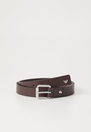 Cinturón de cuero marrón con una hebilla rectangular de plata. Presenta una textura suave y un diseño minimalista. Incluye un pequeño logo en la correa.