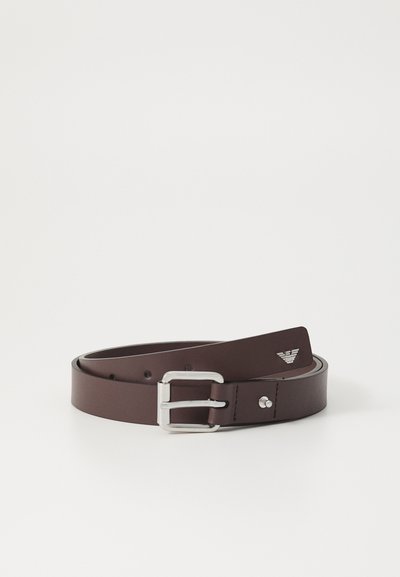 Cinturón de cuero marrón con una hebilla rectangular de plata. Presenta una textura suave y un diseño minimalista. Incluye un pequeño logo en la correa.