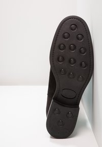 Svart skosula med cirkulära greppmönster, tillverkad av gummi, har rundade kanter och en slät yta, vinklad på en vit yta.