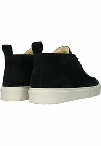 Botas de tobillo de ante negro con un forro interior de felpa y suelas de goma blanca. Presentan costuras sutiles y pestañas en bucle para ponerse y quitarse fácilmente.