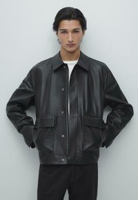 Sort læderjakke med lynlås foran, store lommer og en afslappet pasform. Har en spids krave og knapdetaljer, struktureret finish.