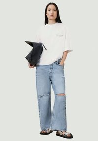 Hvid oversized t-shirt med logo, lyseblå slidte brede jeans, sort taske og sorte sandaler med sølv detaljer.