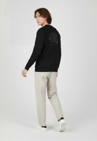 Czarna bluza z subtelną grafiką na plecach, w połączeniu z jasnobeżowymi spodniami i białymi trampkami, prezentująca casualowy, nowoczesny styl.