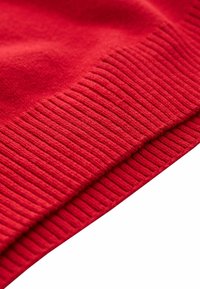 Gros plan sur un tissu tricoté rouge avec une texture côtelée visible le long du bord, montrant des coutures détaillées et un matériau doux.