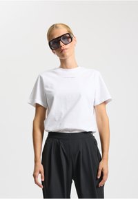 Hvid bomulds t-shirt med korte ærmer, dekoreret med et trykt logo. Kombineret med høj talje sorte bukser, der fremhæver en afslappet pasform.