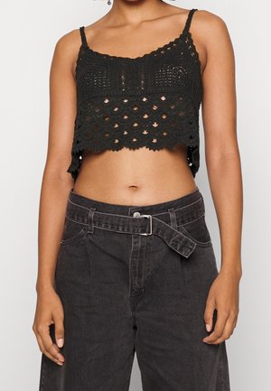 Top noir court avec un design en crochet texturé, doté de fines bretelles et d'un ourlet festonné, associé à un pantalon en denim sombre à taille haute.