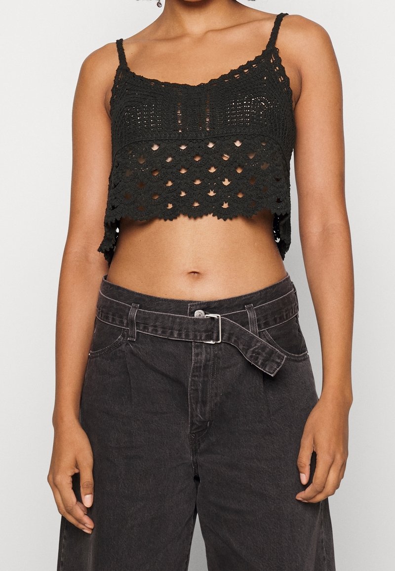 Top noir court avec un design en crochet texturé, doté de fines bretelles et d'un ourlet festonné, associé à un pantalon en denim sombre à taille haute.