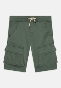 Zelené cargo šortky s velkými předními klopovými kapsami, šikmými předními kapsami a bílou stažitelnou šňůrkou v pase na jednofonním pozadí.