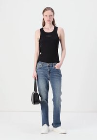 Schwarzes Tanktop, ausgewaschene blaue Jeans, weiße Sneakers, hält eine kleine schwarze Handtasche. Einfaches Design, lässige Passform und grundlegende Stofftexturen.