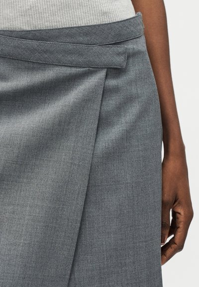Κοντινό πλάνο ενός ατόμου που φοράει γκρι φούστα τύπου wrap με υφή υφάσματος και γκρι ριμπ τοπ που έχει μπει μέσα στη φούστα.