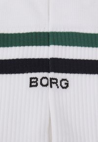 Weiße Socken mit gerippter Textur, die grüne und schwarze Streifen sowie ein schwarzes "BORG"-Logo am Boden aufweisen. Robustes Strickmaterial.