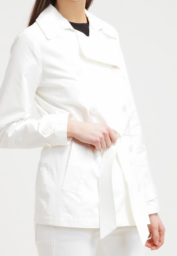 Vit dubbelknäppt jacka med dekorativa knappar och midjeband. Tillverkad av ett slätt tyg, har en klassisk krage och sidofickor.
