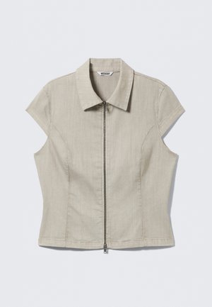 Chemise beige à manches courtes avec col et fermeture éclair centrale, coutures ajustées, et une étiquette indiquant « WEEKDAY » à l'intérieur du col.