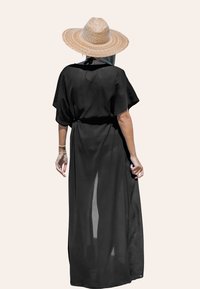 Schwarzes, transparentes Maxikleid mit kurzen Ärmeln, tailliertem Bund und luftigem Schnitt. Kombiniert mit einem breitkrempigen Strohhut.