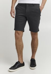 Shorts taillés gris foncé en tissu texturé, avec poches latérales et fermeture à boutons, associés à des baskets noires.