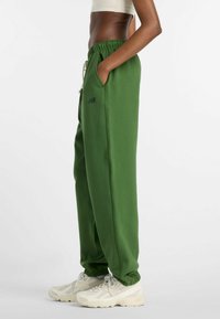 Grüne Jogginghose mit Kordelzugbund, Seitentaschen, gerippten Bündchen und einem kleinen schwarzen Logo, kombiniert mit hellen Sneakern.