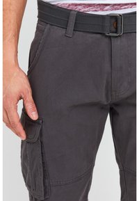 Man wearing dark gray cargo pants with a matching fabric belt, hand resting near the side pocket flap.