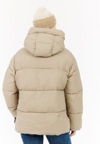 Beige pufferjack met capuchon, voorzien van een quilted ontwerp, zachte textuur en een losse pasvorm. Draagt een lichtbeige gebreide beanie.