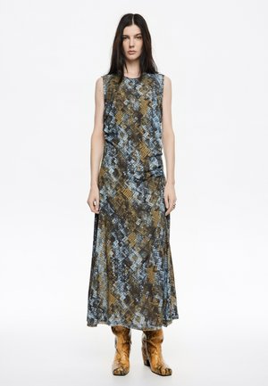 Stijlvolle mouwloze maxi-jurk in blauw en bruin met een geometrisch patroon, met een relaxte pasvorm en een soepele stoftextuur. Draagt met gestructureerde brownschoenen.