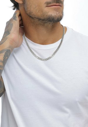 Silberne Kettenhalskette mit klassischem Panzerkettendesign, getragen über einem schlichten weißen T-Shirt, die Struktur und den Glanz des Metalls zeigend.