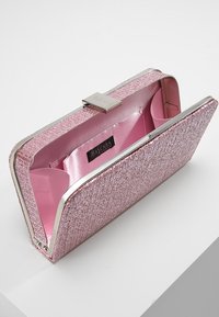 Clutch-väska i rosa skimrande tyg med strukturerad yta, silverfärgade detaljer och satinrosa inredning. Har en magnetisk stängning och ett innerfack.