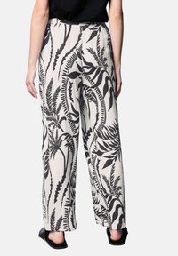 Losse, lichte broek met een zwart-wit bladpatroon; geweven textuur met een elastische tailleband. Zacht materiaal voor comfort.